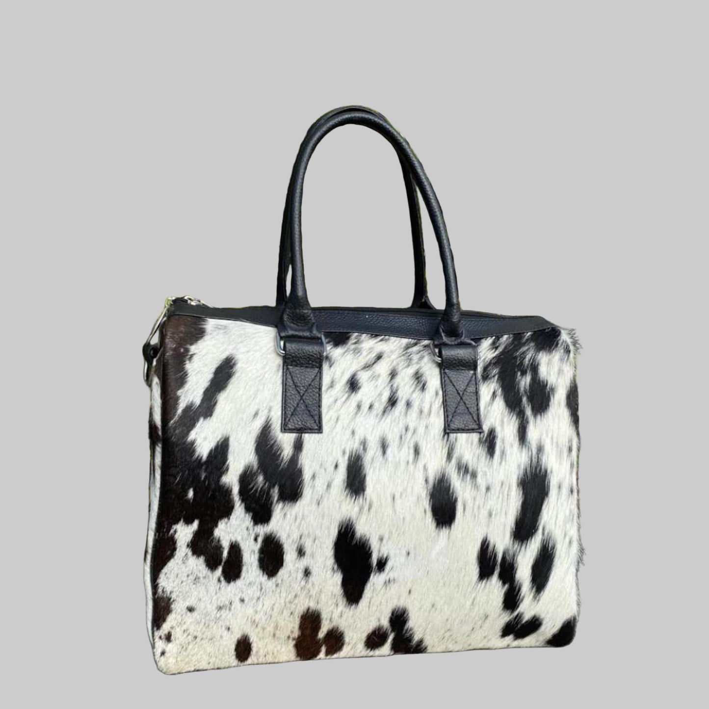 Black and white cow print handbag with black handles against a green plant background