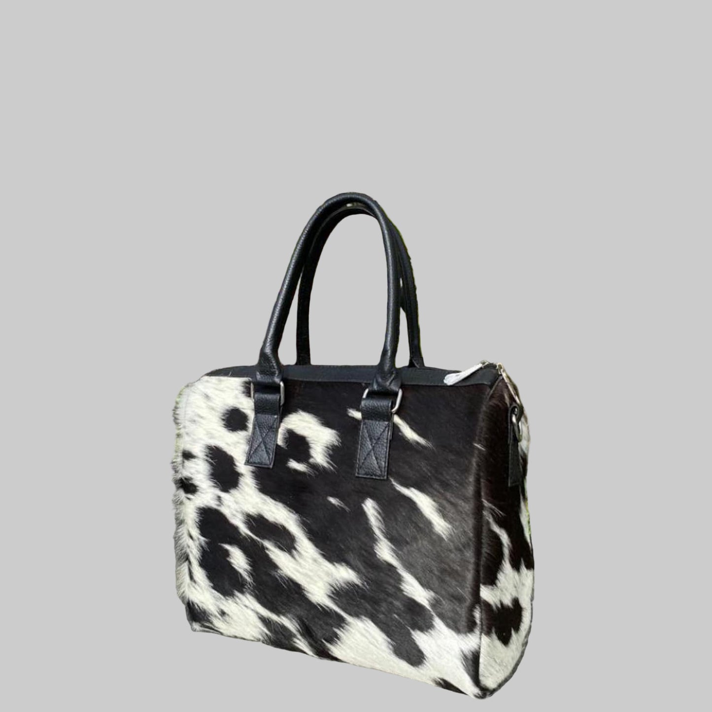 Black and white cowhide handbag on a stone surface with plants in the background