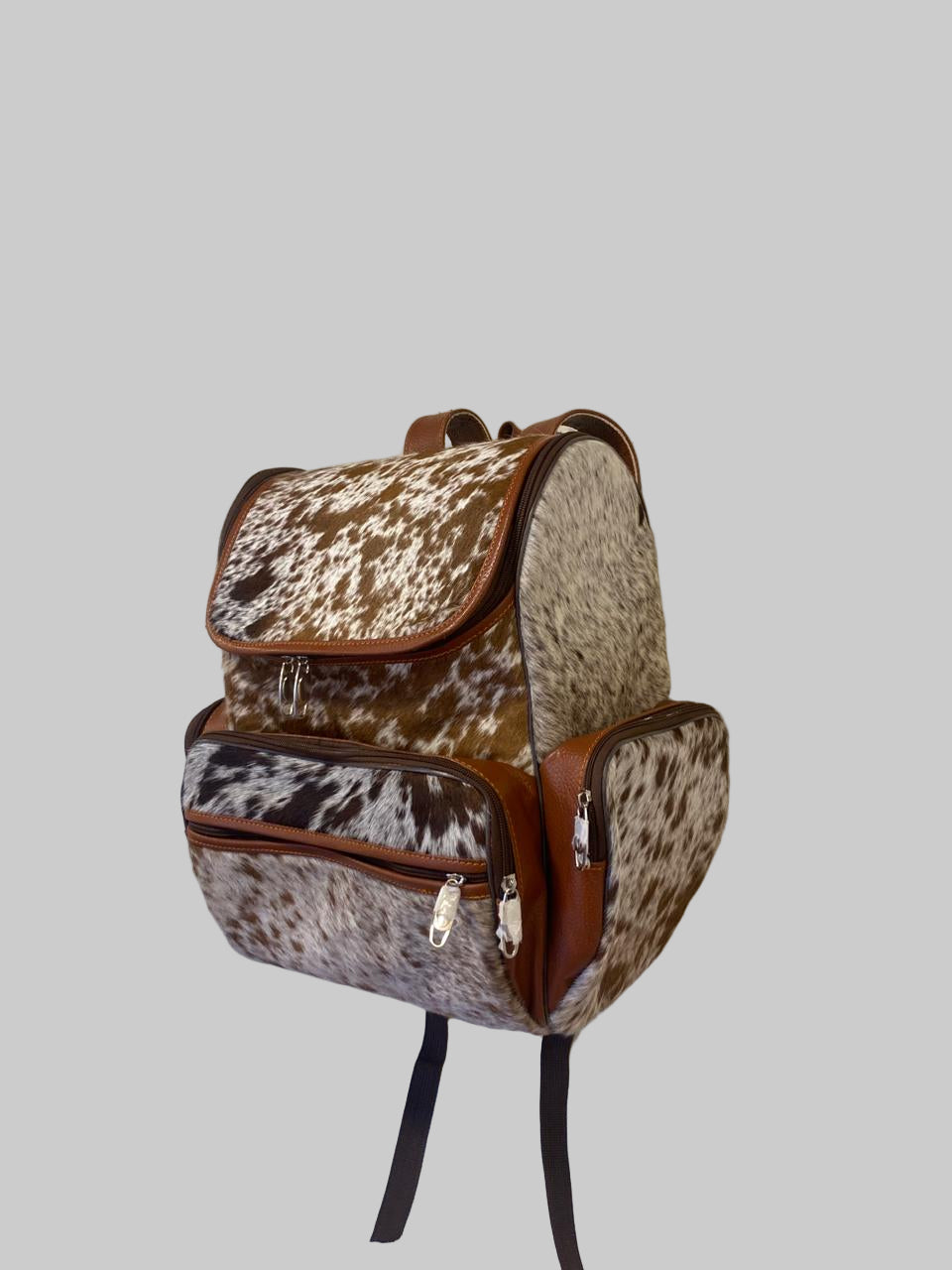 Backpack with cow print pattern hanging on a textured wall.