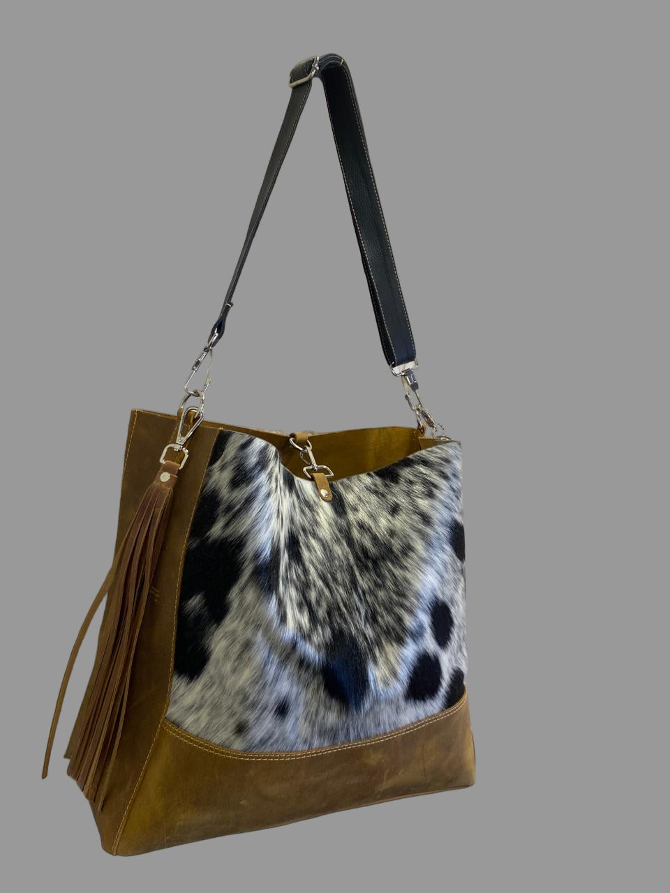 Handbag with a cowhide pattern and brown leather accents against a decorative wall.