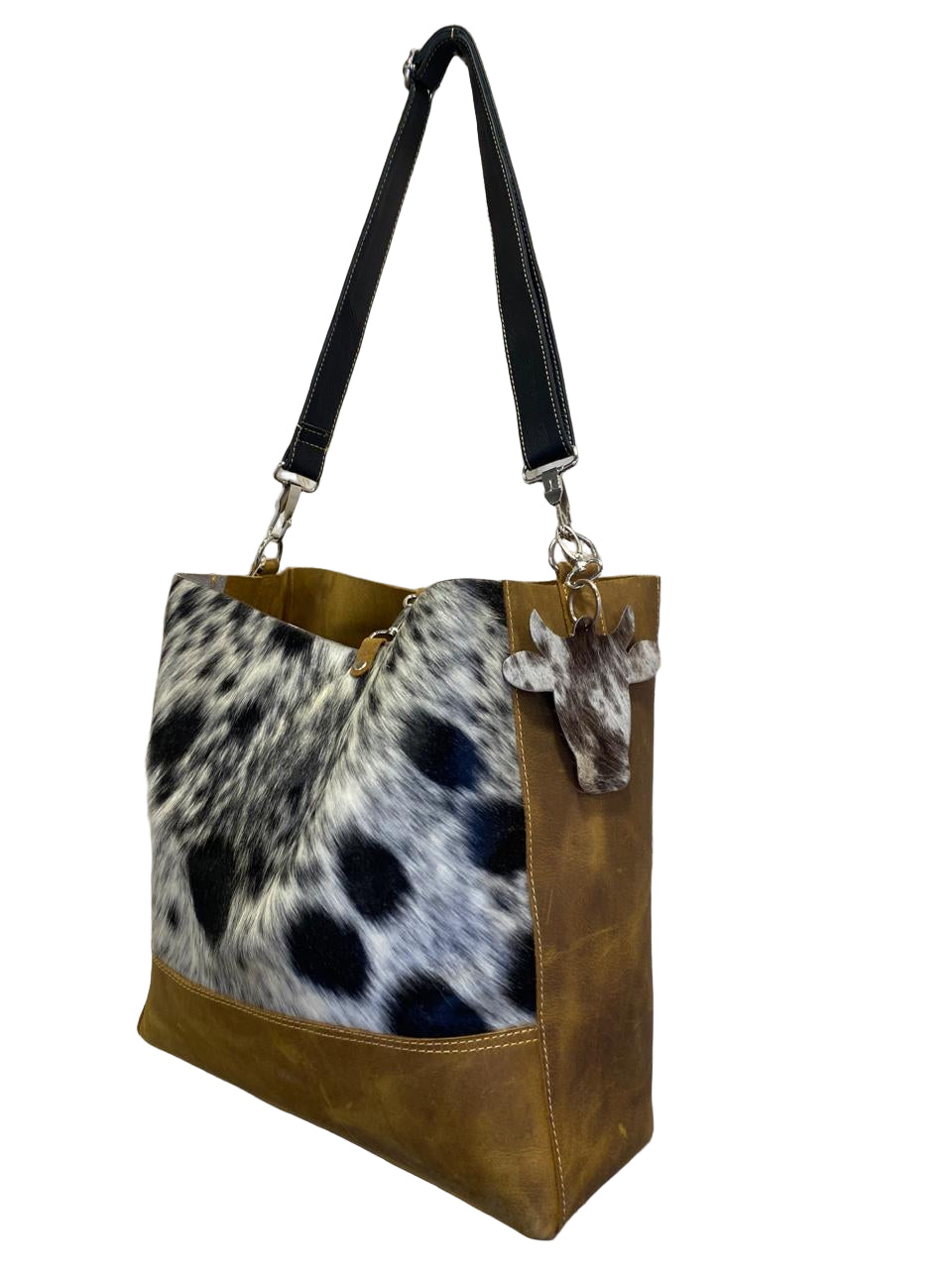 Handbag with cowhide pattern and leather accents on a decorative wall.