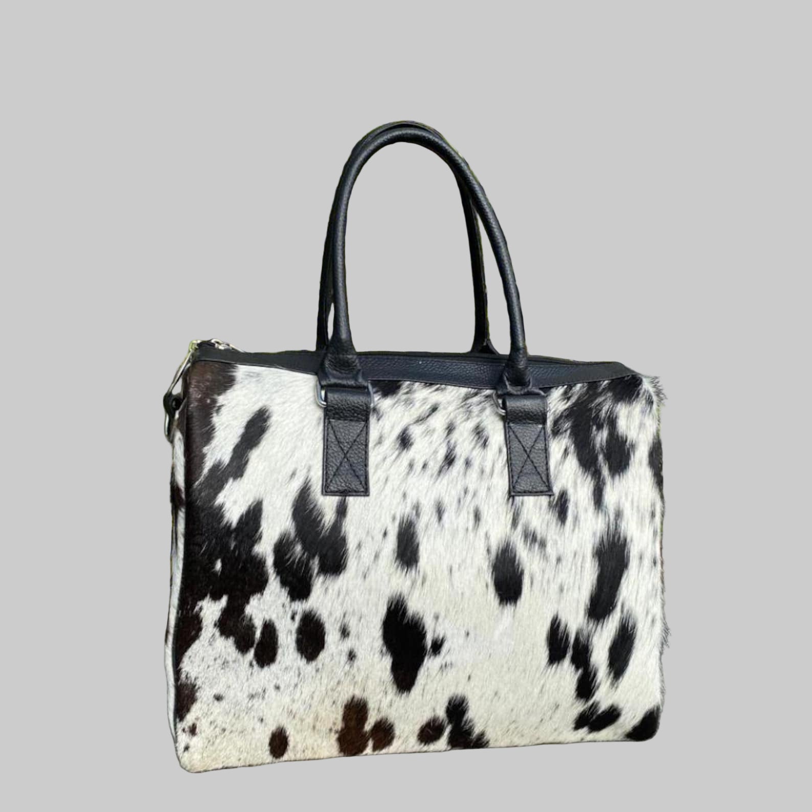 Black and white cow print handbag with black handles against a green plant background