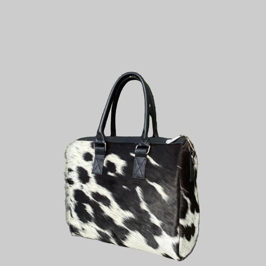 Black and white cowhide handbag on a stone surface with plants in the background